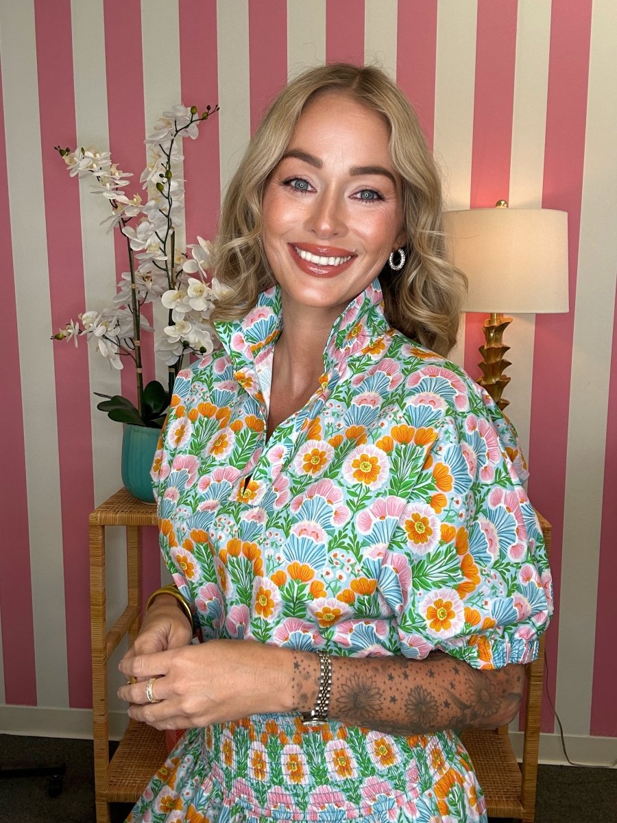 Woman wearing a colorful floral dress in a room with striped wallpaper.