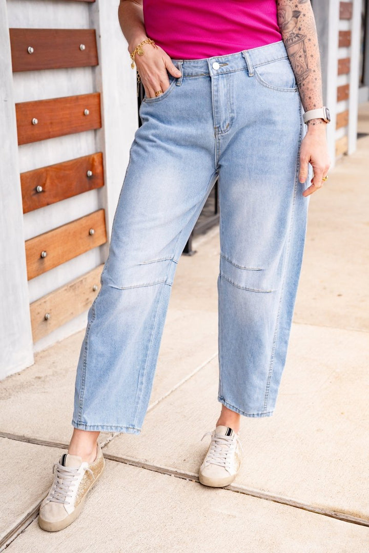 Person wearing light blue jeans and a pink top, standing on a sidewalk.