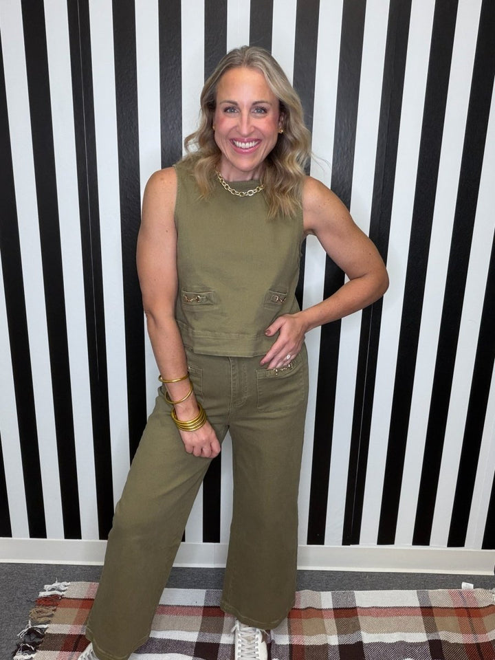 A woman modeling an olive green sleeveless crop top and matching wide-leg pants, standing in front of a black and white striped wall.