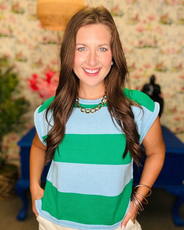 Woman wearing a green and blue striped shirt with a floral wall in the background