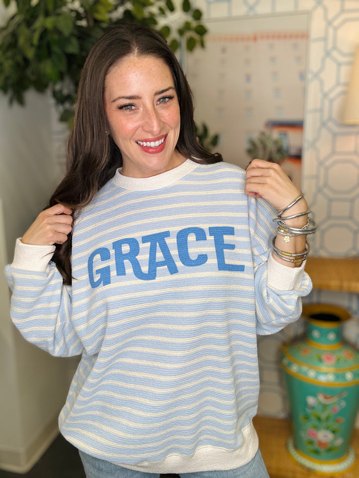 Woman wearing a blue and white striped shirt with 'GRACE' printed on it, standing indoors.