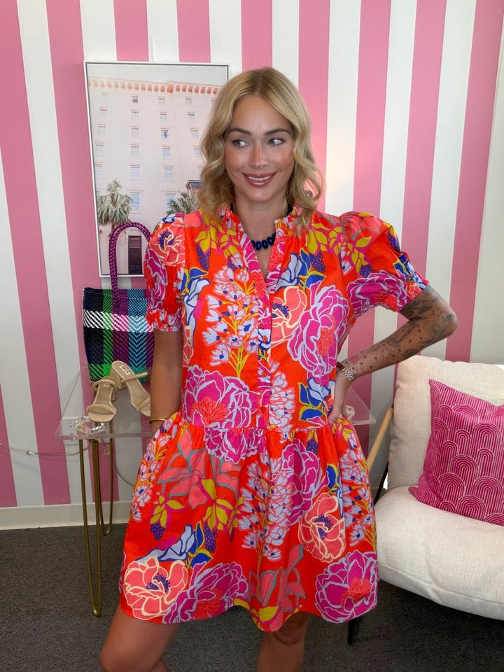Woman in a colorful dress standing in a room with pink and white striped walls.