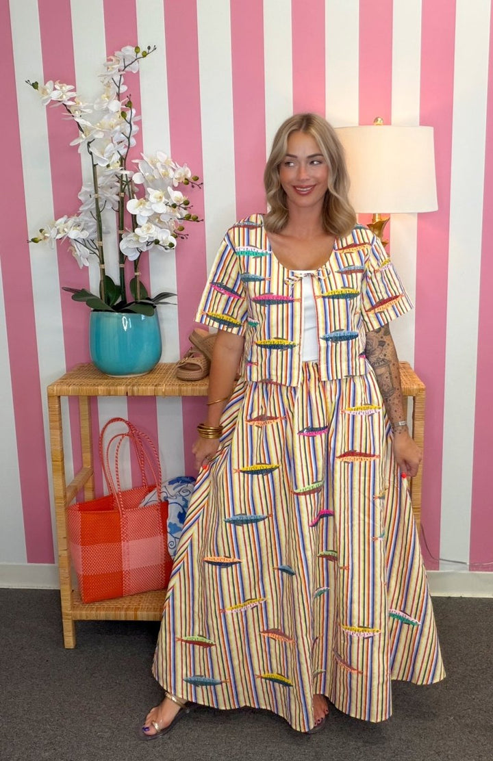 Woman wearing a colorful dress standing in front of a pink and white striped wall.