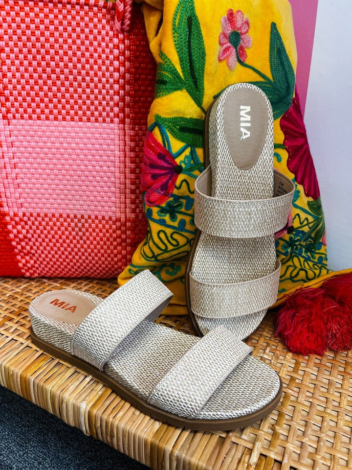 Pair of silver sandals with 'MIA' branding on a woven surface with colorful background