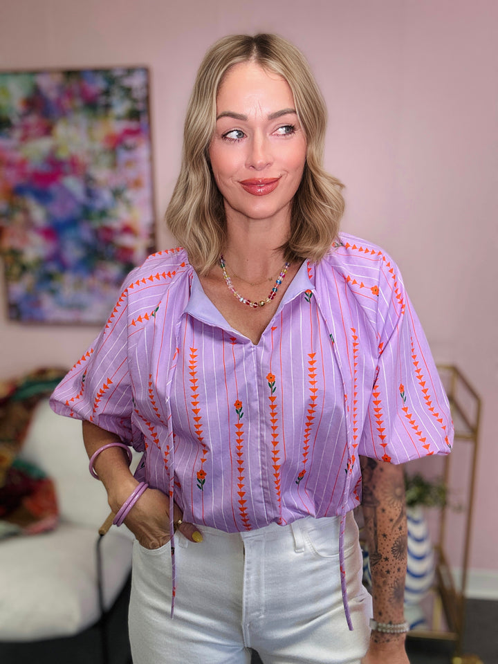 Woman wearing a patterned blouse in a room with colorful decor
