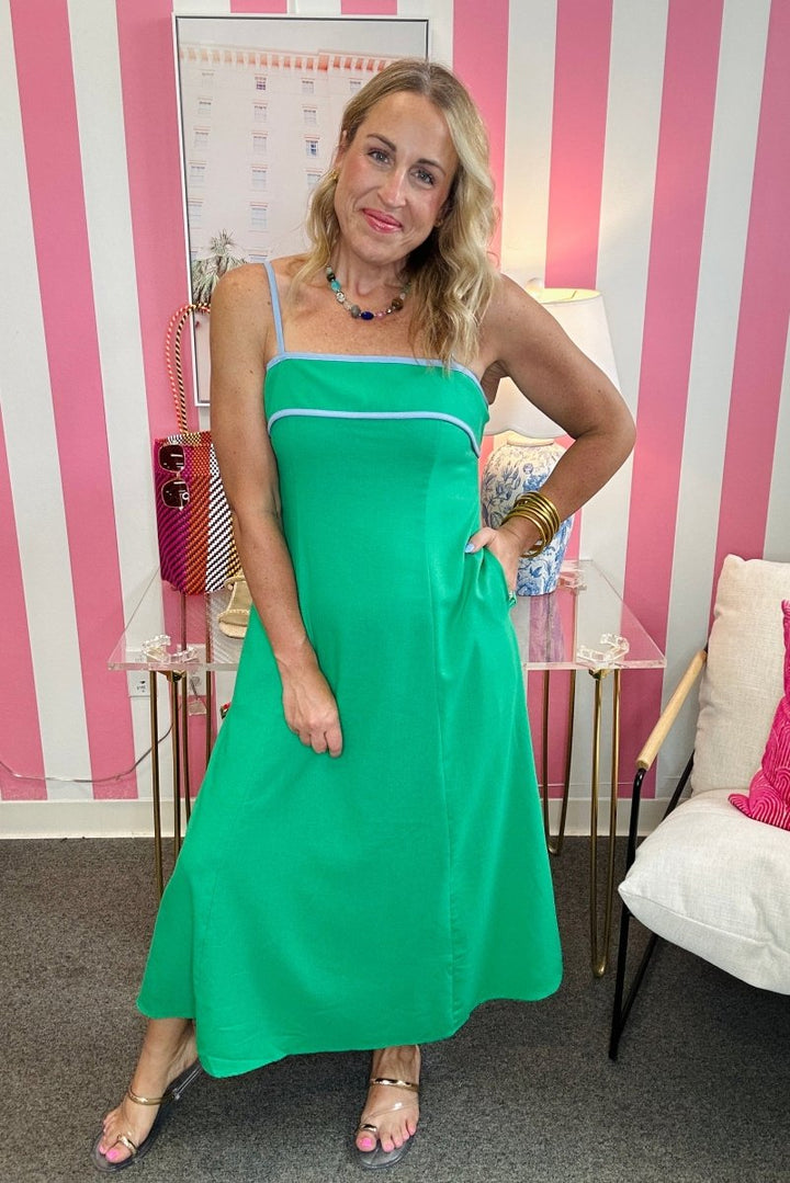 Woman in a green dress standing in a room with pink and white striped walls.