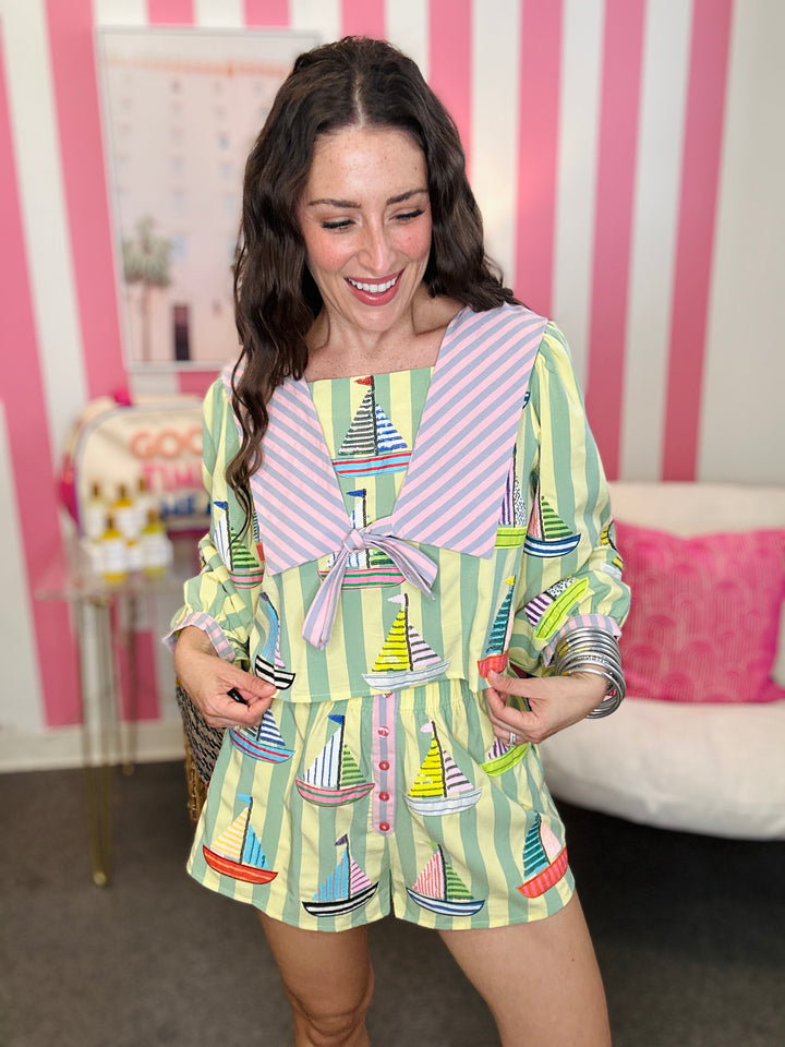 Woman wearing a colorful outfit with sailboat pattern in a room with pink and white striped walls.