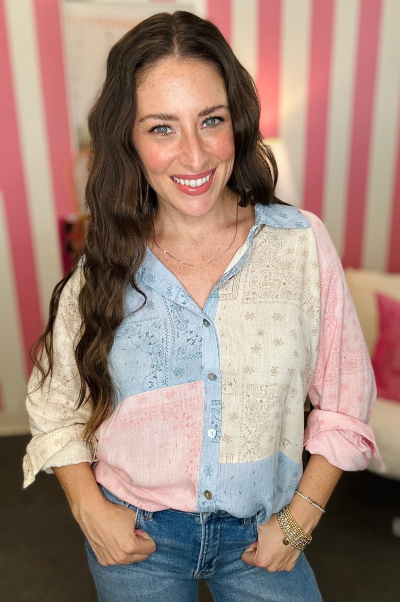 Woman wearing a patterned shirt with rolled-up sleeves in front of a striped wall.