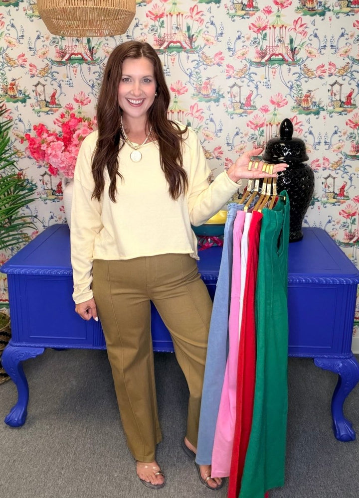 Woman standing next to a rack of colorful dresses against a floral-patterned wall.