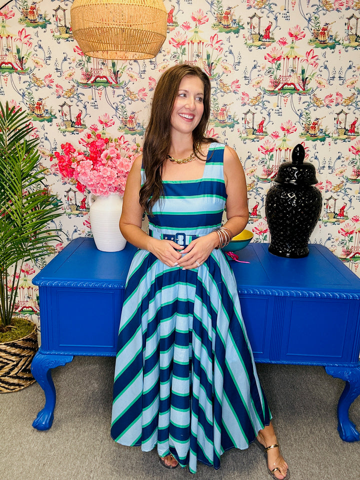 Woman in a striped dress sitting on a blue bench against a floral wall.