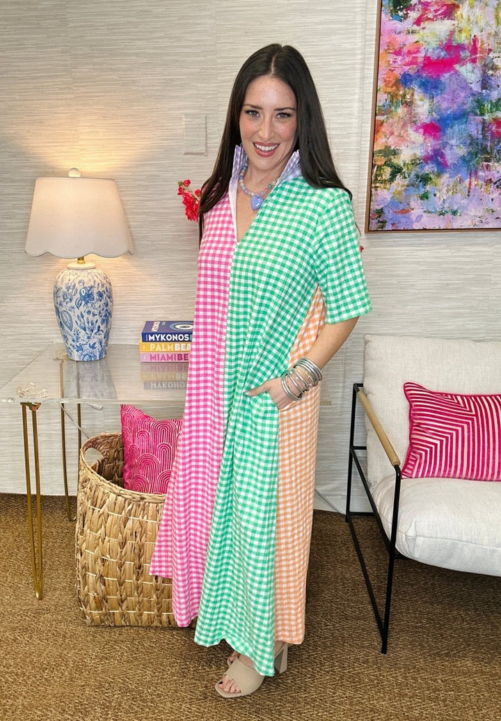 Woman in a colorful checkered dress standing in a room with decorative pillows and a lamp.