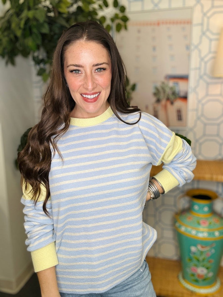 Woman wearing a blue and yellow striped sweater in a room with decorative elements.