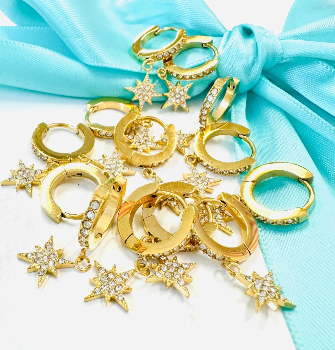 Gold hoop earrings with star-shaped charms on a turquoise fabric background