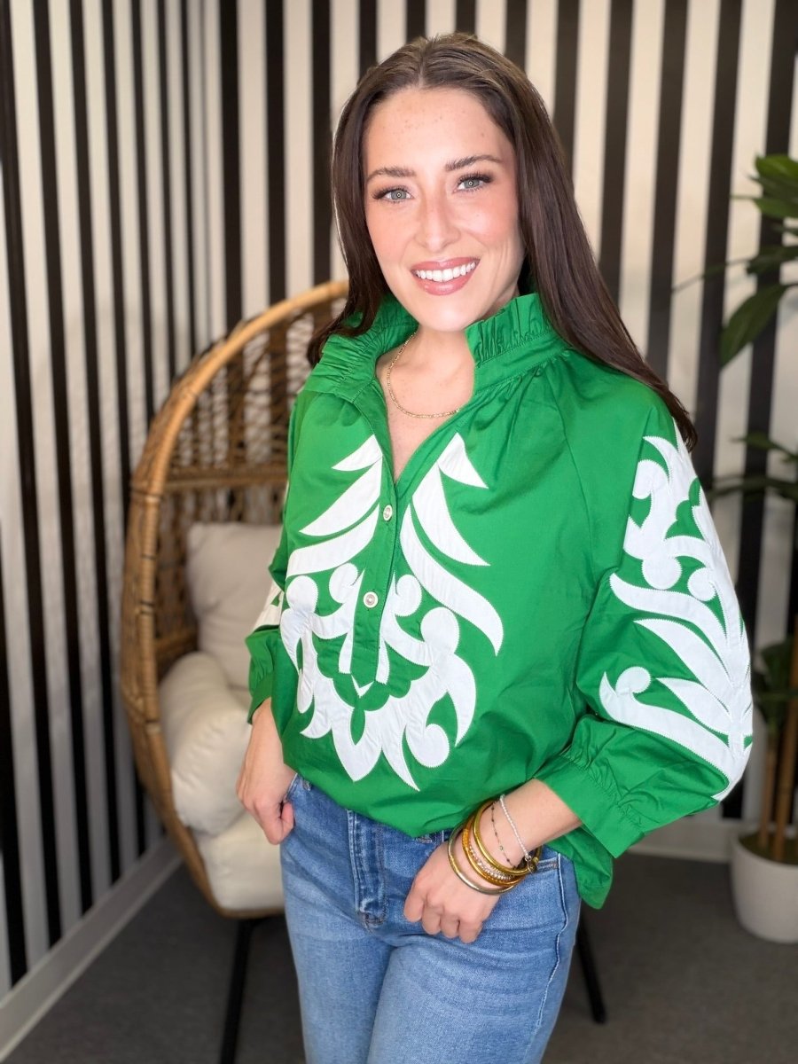 Woman wearing a green jacket with white patterns in a room with striped walls and a wicker chair.