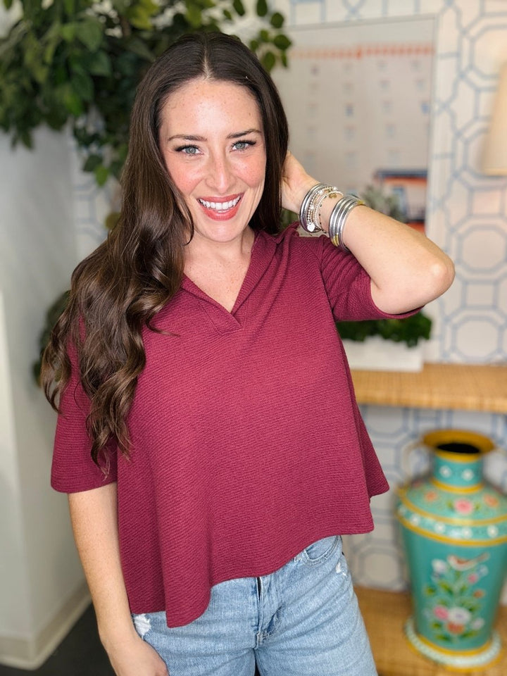 Woman wearing a maroon top and light blue jeans indoors with decorative elements.