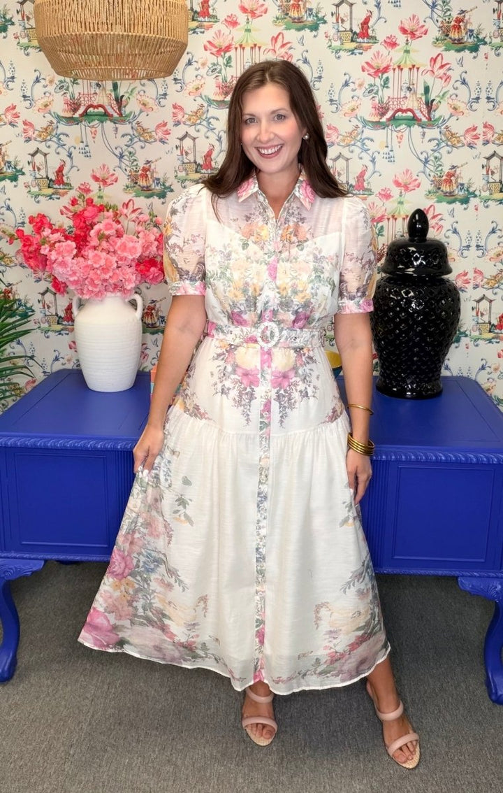 Woman in a floral dress standing in front of a colorful wall with decorative elements.