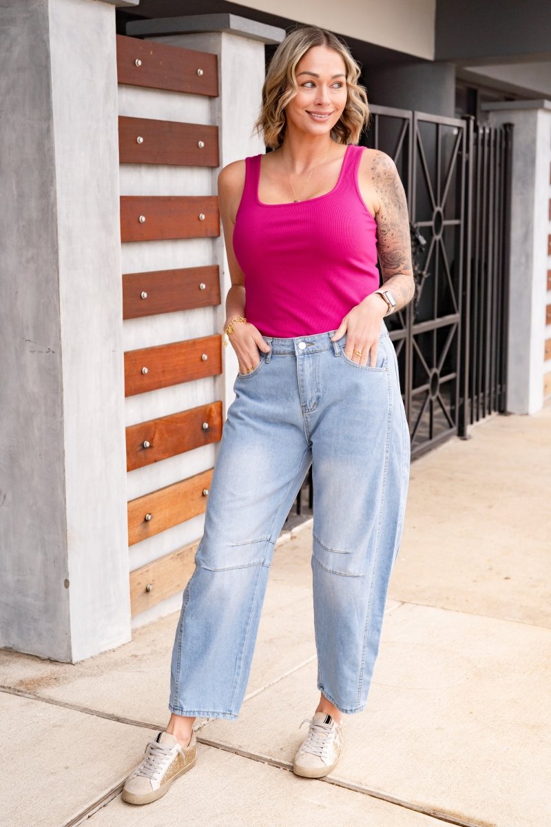 Woman wearing a pink tank top and light blue jeans standing against a modern building.