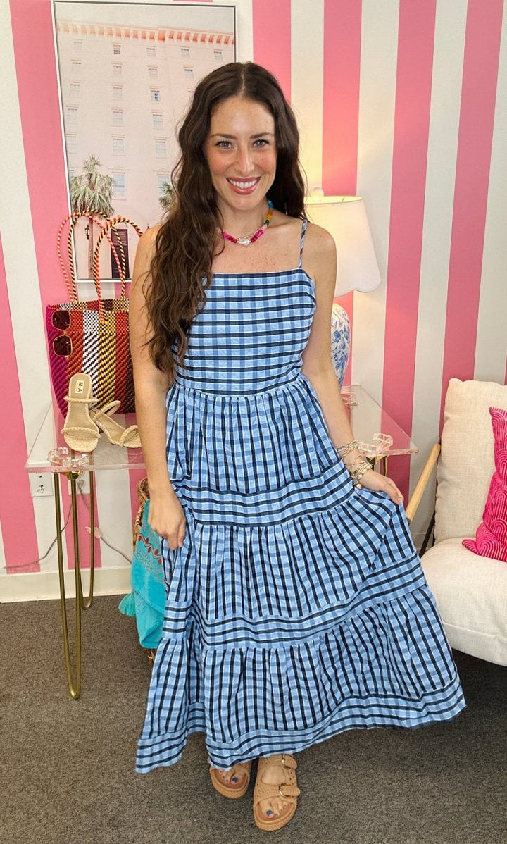 Woman wearing a blue checkered dress in a room with striped walls and furniture.
