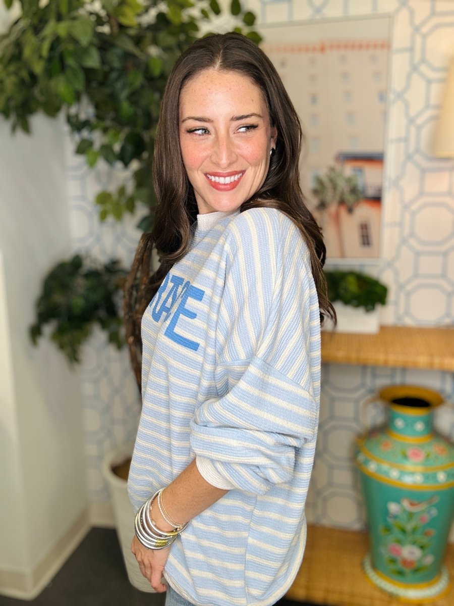 Woman wearing a blue and white striped shirt with 'GRACE' printed on it, standing indoors.