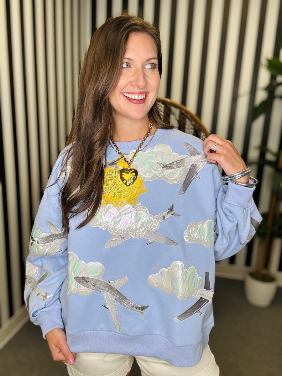 Woman wearing a blue sweatshirt with airplane and cloud patterns indoors.