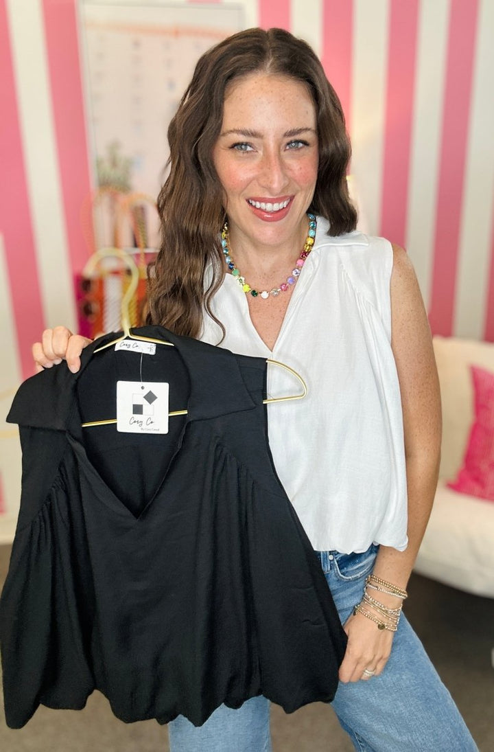 Woman holding a black top with a visible brand label against a striped curtain background