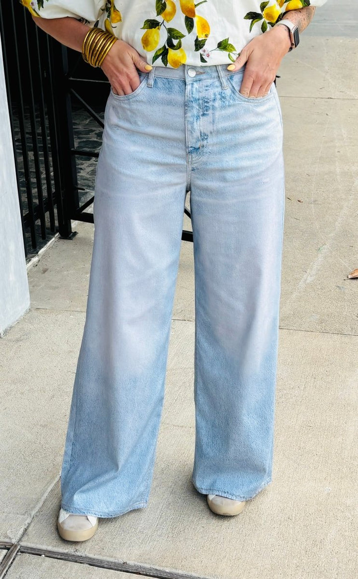 Person wearing light blue jeans and a floral top on a sidewalk.