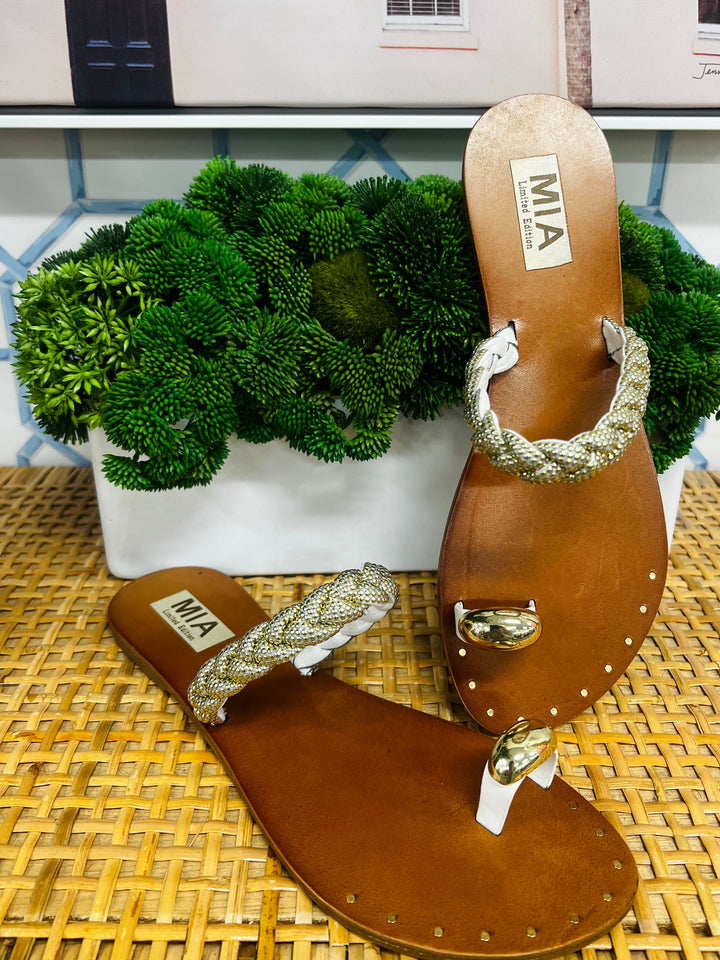 Brown sandals with braided straps on a woven surface with a plant in the background