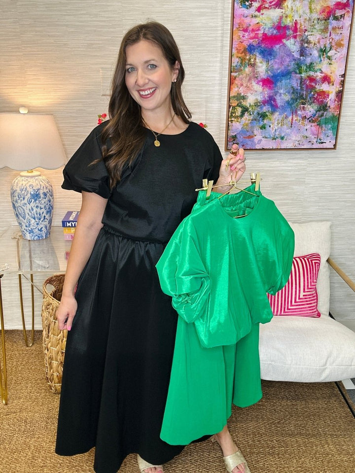 Woman holding a green outfit in a room with a colorful painting on the wall.