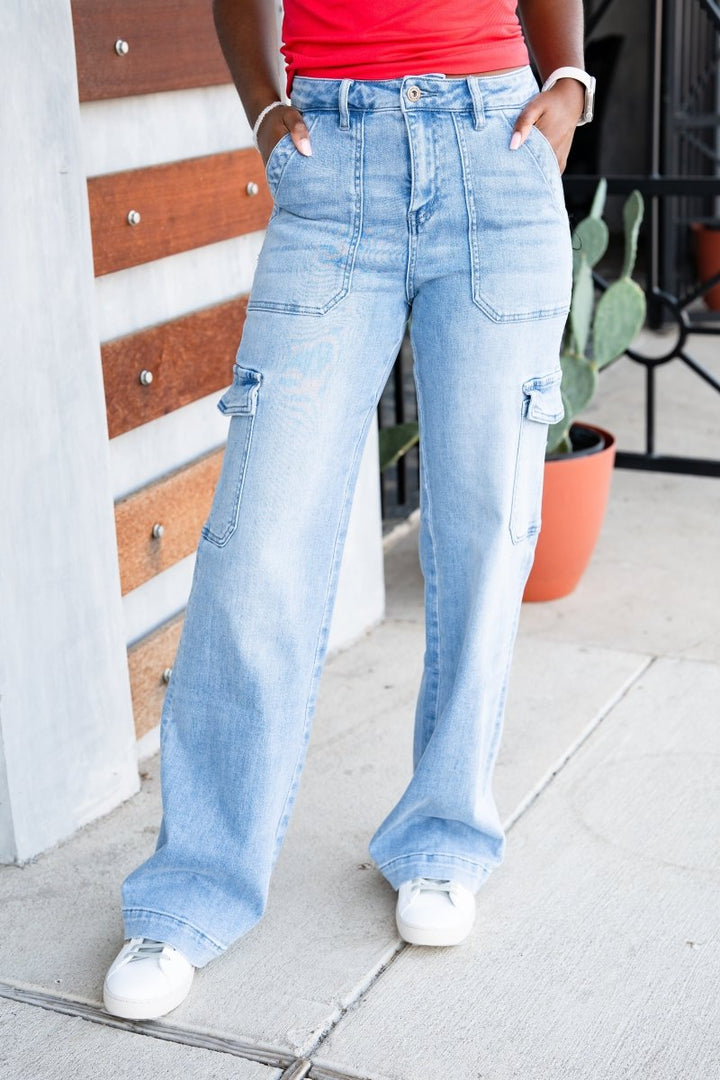 Person wearing light blue jeans with a red top and white sneakers, standing on a sidewalk.