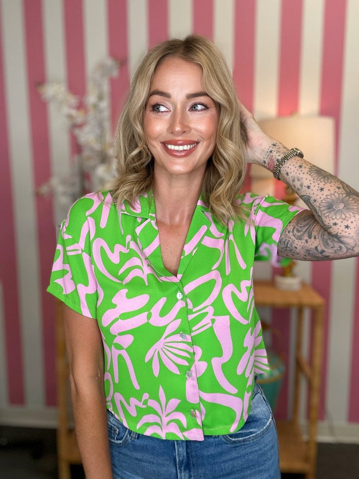 Woman wearing a green and pink patterned shirt in a room with striped wallpaper.