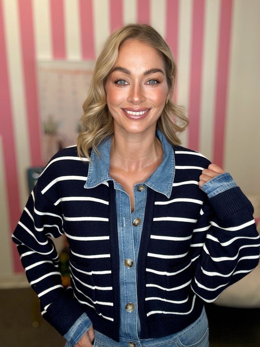 A woman wearing a navy and white horizontally striped knit cardigan with a light blue denim collar and button-front placket, standing in front of a pink and white striped wall.