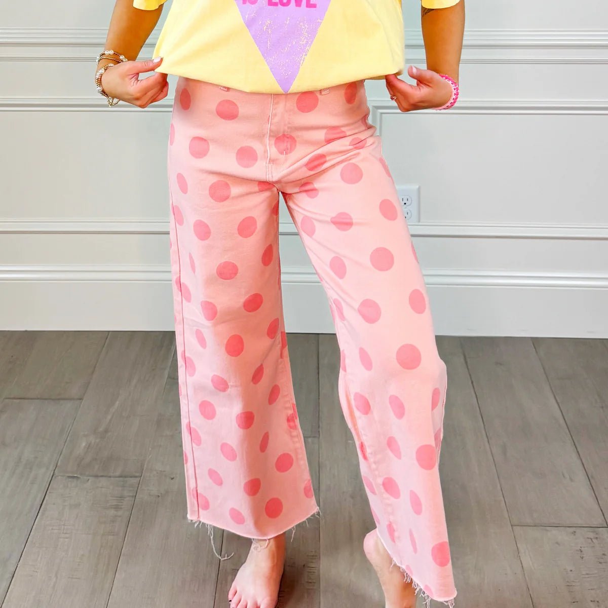 Person wearing a colorful top and pink polka dot pants in a room with wooden flooring.