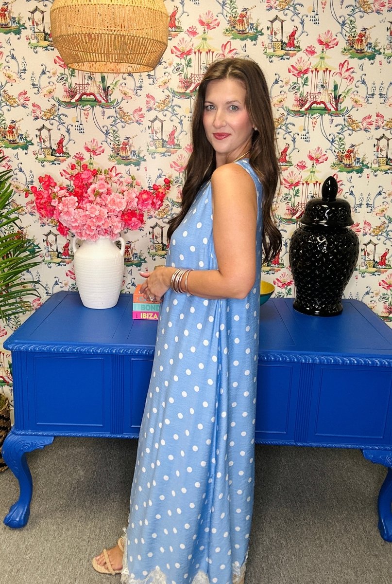 Woman in a blue polka dot dress standing in front of a colorful wall with floral patterns.