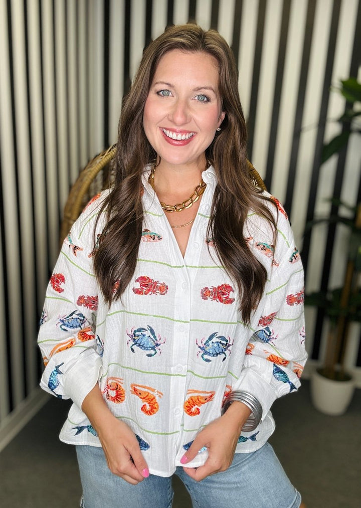 Woman wearing a white blouse with colorful sea-themed designs indoors.