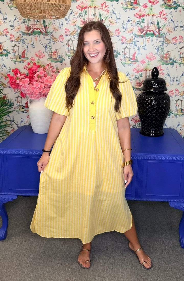 Woman in a yellow dress standing in front of a colorful floral-patterned wall.