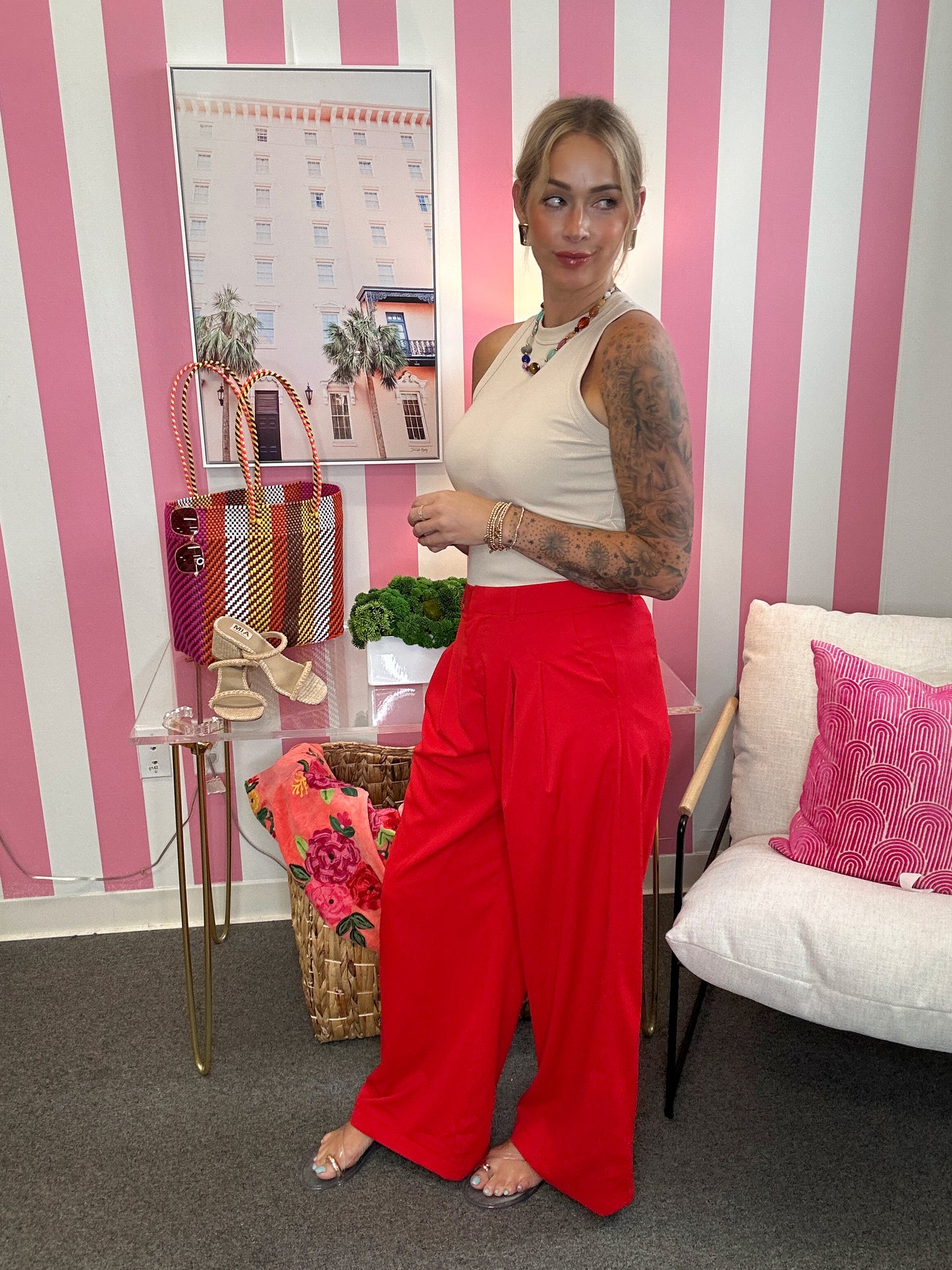 Woman in a white top and red pants standing in a room with striped walls and decorative items.