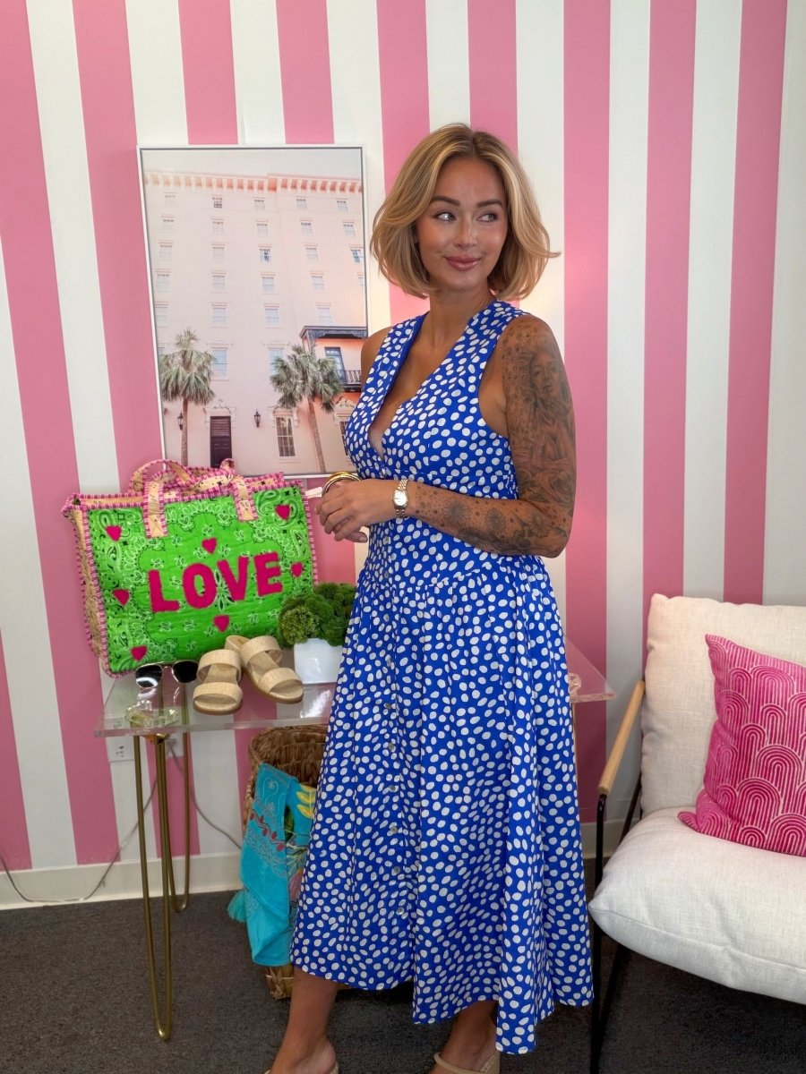 Woman in a blue dress standing in a room with pink and white striped walls, a green bag, and a couch.