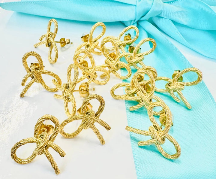 Gold bow-shaped earrings on a light blue fabric background