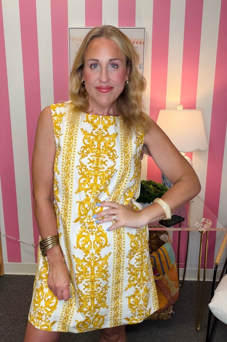 Woman wearing a yellow and white patterned dress in front of a striped wall.