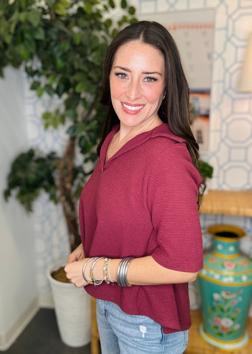 Woman wearing a maroon top with a plant and decorative vase in the background