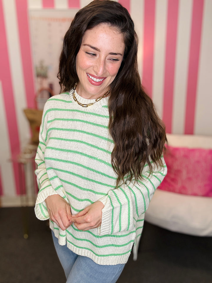 Woman wearing a green and white striped sweater in front of a pink and white striped wall.
