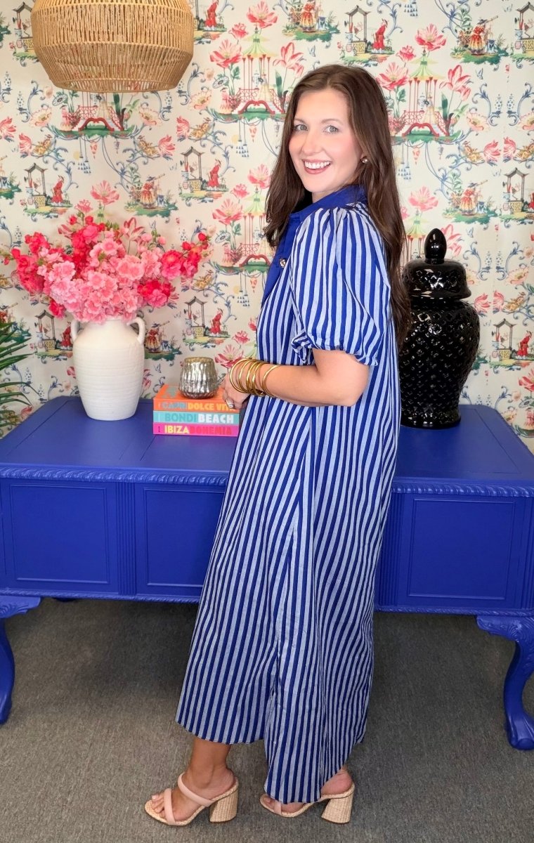 Woman in a blue and white striped dress standing in a room with colorful wallpaper and furniture.