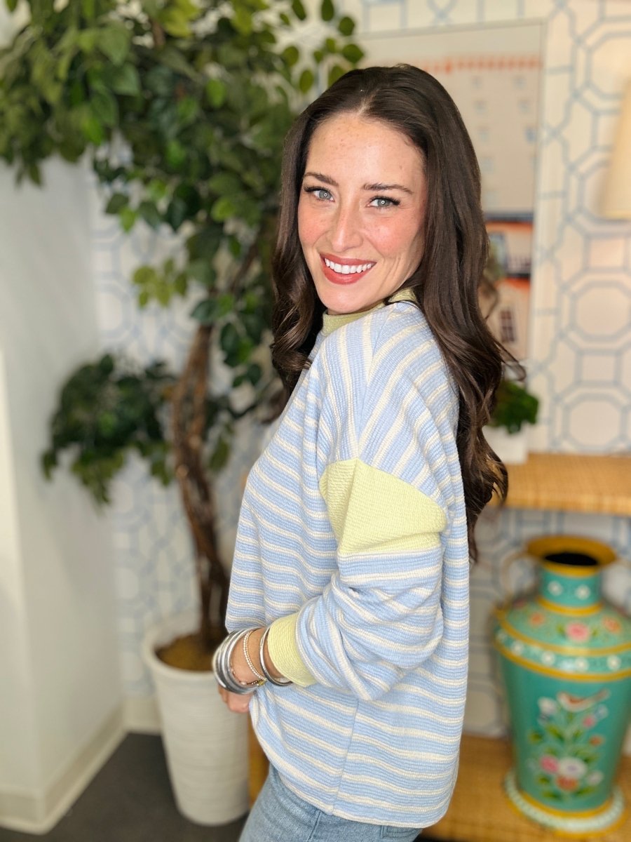 Woman wearing a light blue and yellow striped sweater in a room with plants and decor.