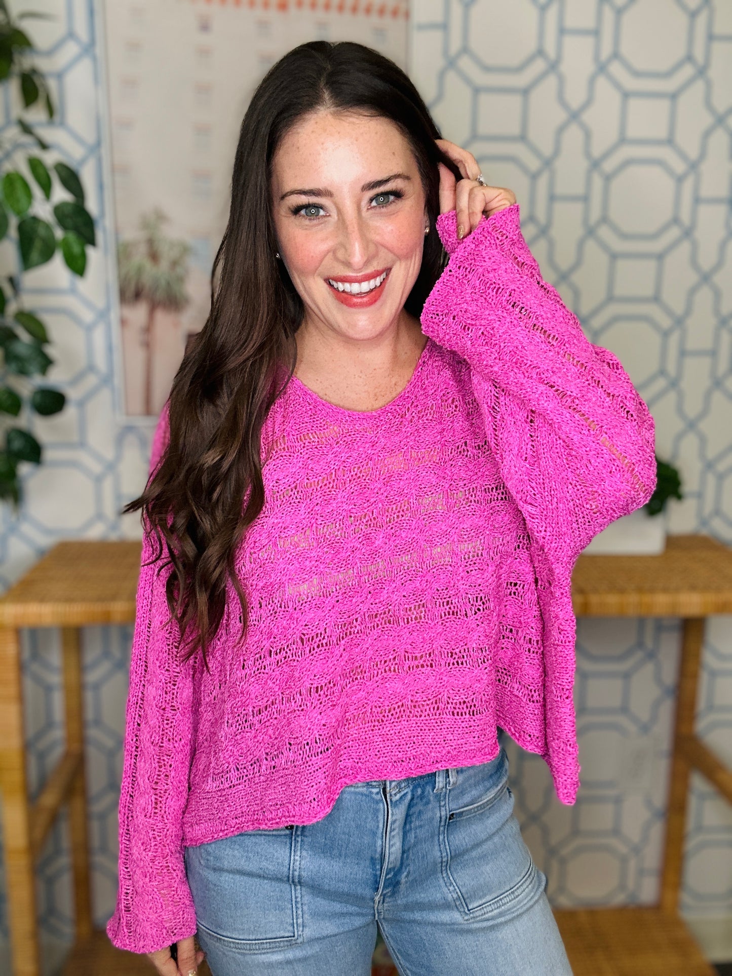 Woman wearing a pink sweater and blue jeans indoors with a decorative wall in the background