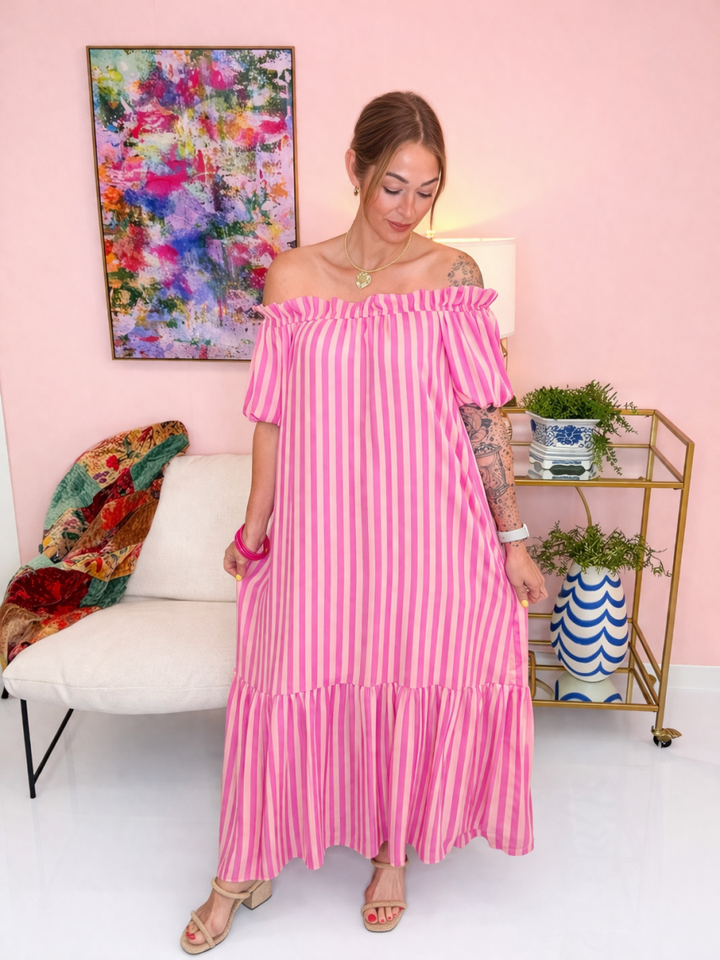 Woman wearing a pink striped dress in a room with a colorful painting and a plant.