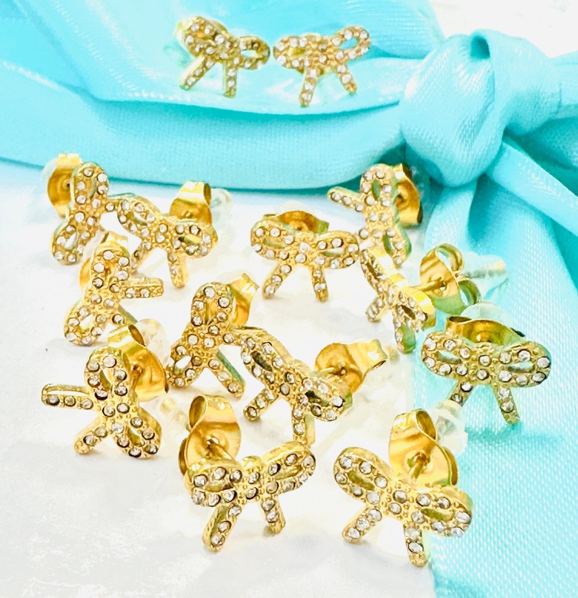 Gold bow-shaped earrings on a light blue fabric background