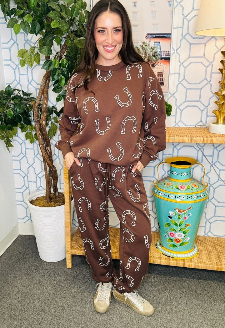 Woman wearing a brown outfit with horseshoe patterns in a room with decorative elements.