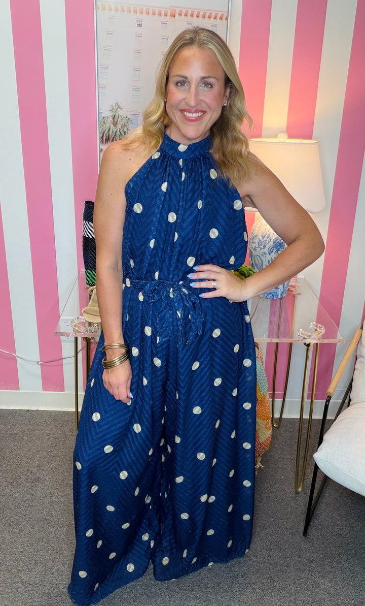 Woman wearing a blue polka dot dress in an indoor setting with striped walls.