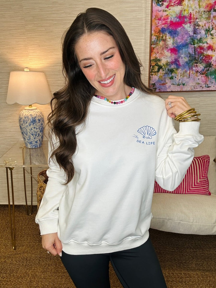 Woman wearing a white sweatshirt with a logo in a living room setting