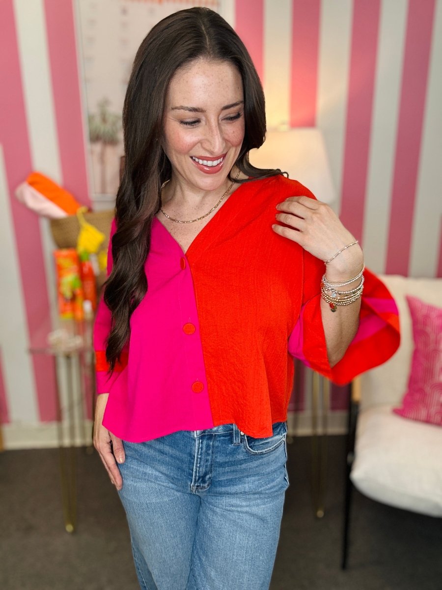 Woman wearing a colorful two-tone top with a striped wall in the background